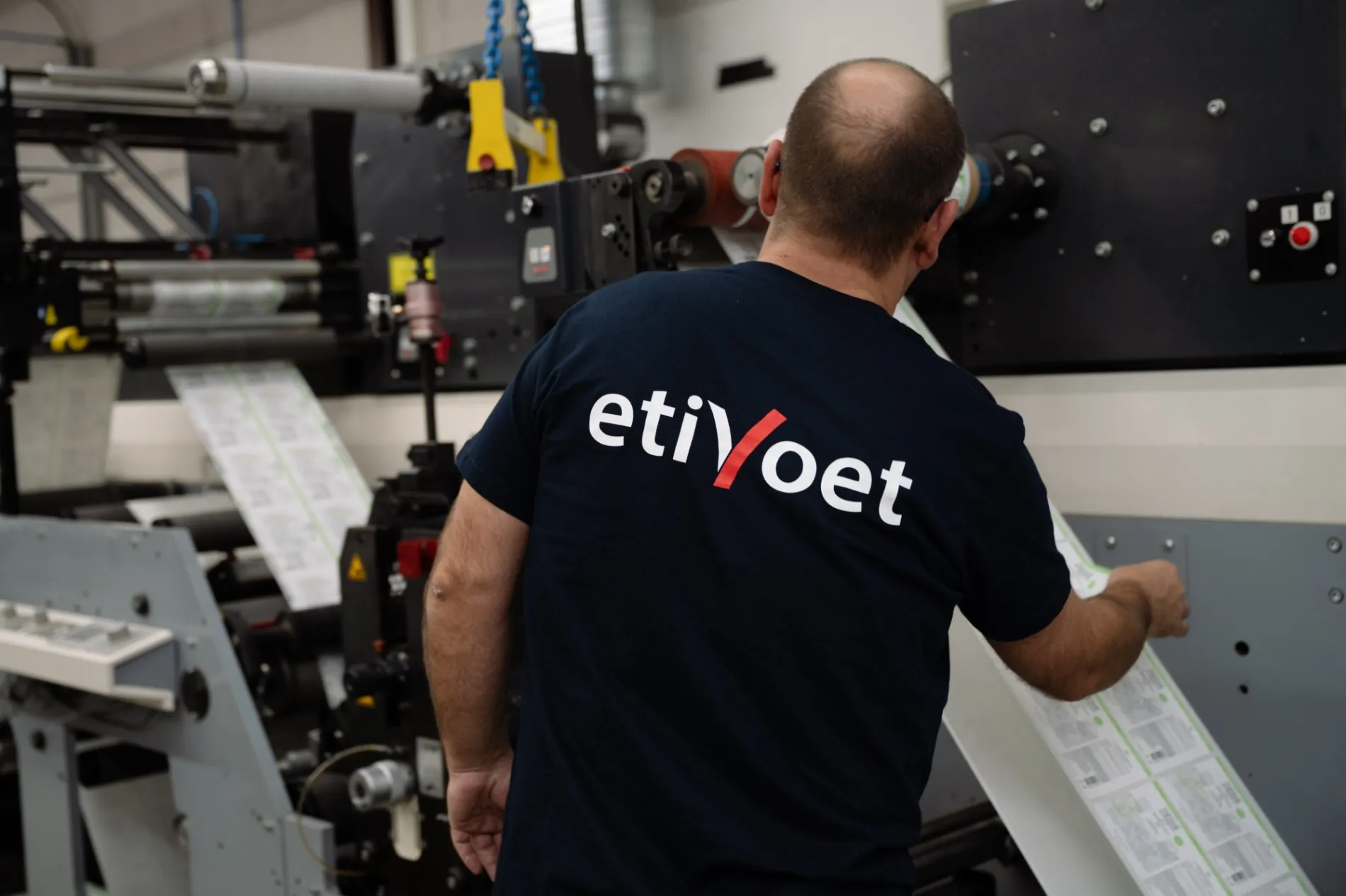 Medewerker van Etivoet controleert de productie van zelfklevende etiketten op een industriële etikettendrukpers.